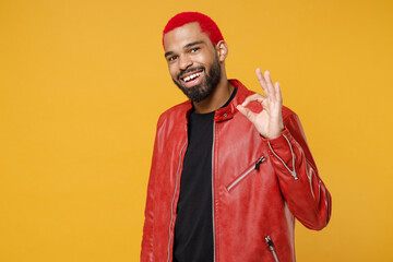 Wall Mural - Young african dark-skinned happy smiling man 20s with funky trendy pink hairdo wearing stylish red leather jacket showing ok okay gesture isolated on yellow orange color background studio portrait.