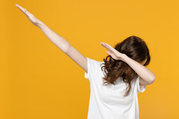 Wall Mural - Young fun student cool woman 20s wearing white casual t-shirt doing dab hip hop dancing hands move gesture youth sign hiding covering face isolated on yellow orange color background studio portrait.