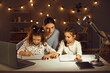 © Studio Romantic - Family doing homework sitting at desk late in the evening. Focused mother and concentrated little kids working on school assignments together. Parent helping children to draw and write in copybooks