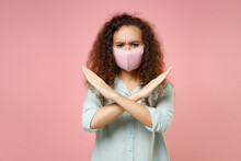 Young Black African Curly Strict Woman In Blue Shirt Reusable Face Mask From Coronavirus Covid-19, Pandemic Quarantine Do Stop Gesture Crossed Hands Isolated On Pastel Pink Background Studio Portrait.