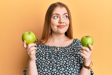 Sticker - Young beautiful redhead woman holding green apples smiling looking to the side and staring away thinking.