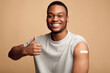 © Prostock-studio - Vaccinated Guy With Plaster On Arm Gesturing Thumbs-Up, Beige Background