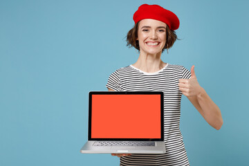 Wall Mural - Young freelancer woman 20s, short hairdo in french beret red hat striped t-shirt hold laptop pc computer, blank screen workspace area show thumb up gesture isolated on blue background studio portrait.