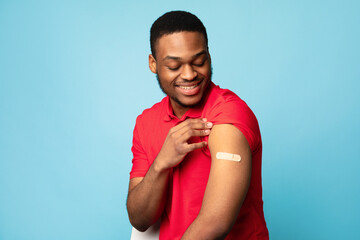 Covid-19 Vaccinated African Guy Showing Arm After Injection, Blue Background