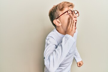 Wall Mural - Little caucasian boy kid wearing casual clothes and glasses shouting and screaming loud to side with hand on mouth. communication concept.