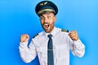 © Krakenimages.com - Handsome man with beard wearing airplane pilot uniform celebrating surprised and amazed for success with arms raised and open eyes. winner concept.