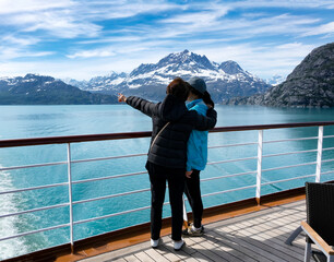 mother holding her daughter while pointing to mountains and glaciers in alaska while on ship