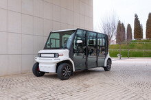 Electric Street Vehicle With Zero Emission Stands Near The Wall In The Park. The Road Is Paved With Cobblestones. Compact Electric Utility Vehicle To Transport Guests To And From An Event.