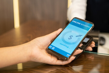 Wall Mural - Hand of young female traveler holding smartphone with online banking page on screen over payment machine standing on reception counter