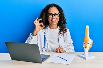 Sticker - Beautiful middle age woman doctor at orthopedic clinic smiling positive doing ok sign with hand and fingers. successful expression.