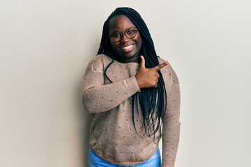 Wall Mural - Young black woman with braids wearing casual clothes and glasses cheerful with a smile of face pointing with hand and finger up to the side with happy and natural expression on face