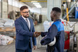© pressmaster - Young elegant businessman in suit and eyeglasses shaking hand of African worker of large industrial plant after making deal and signing contract
