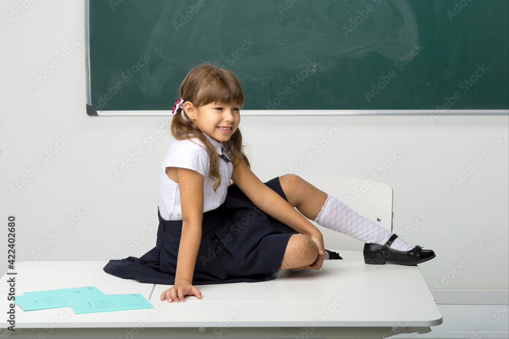 Happy school girl sitting on desk in classroom Stock Photo | Adobe Stock