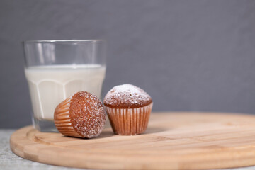 two little cupcakes or muffins in powdered sugar near a glass of milk. healthy breakfast. snack or lunch