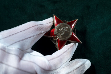 Red Star Order of the World War two in the hand of Expert wearing white canvas gloves against green velvet surface.