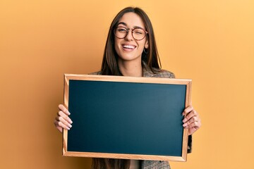 Canvas Print - Young hispanic girl holding blackboard winking looking at the camera with sexy expression, cheerful and happy face.