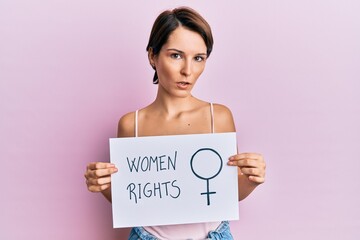 Wall Mural - Young brunette woman with short hair holding woman rights banner clueless and confused expression. doubt concept.