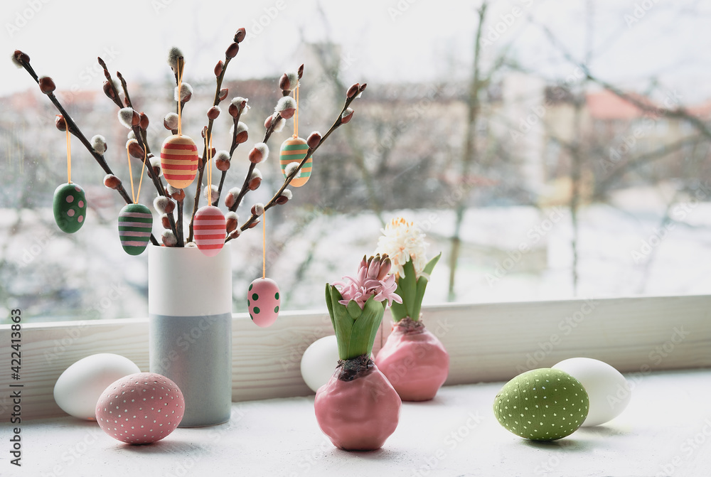 Easter decorations on windowsill, panoramic image. Wooden painted eggs on pussy willow. Hyacinth flowers with bulbs in pink wax. Window, view over town. Romantic indoor setup. Happy Easter - obrazy, fototapety, plakaty 