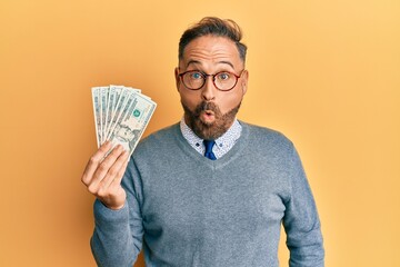 Poster - Handsome middle age man holding 20 dollars banknotes scared and amazed with open mouth for surprise, disbelief face