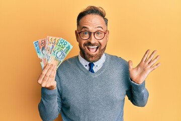 Sticker - Handsome middle age man holding australian dollars celebrating achievement with happy smile and winner expression with raised hand