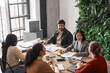 © Seventyfour - High angle portrait of elegant Asian businesswoman talking to group of people during business meeting at table in office, copy space
