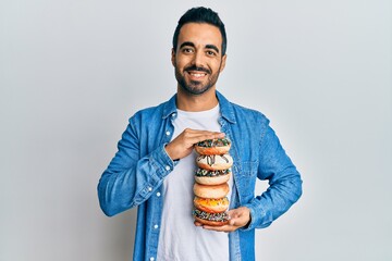 Canvas Print - Young hispanic man holding tasty colorful doughnuts smiling with a happy and cool smile on face. showing teeth.