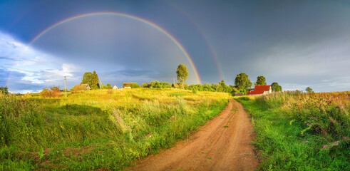 Wall Mural - Rainbow over stormy sky. Rural landscape with rainbow over dark stormy sky in a countryside at summer evening.