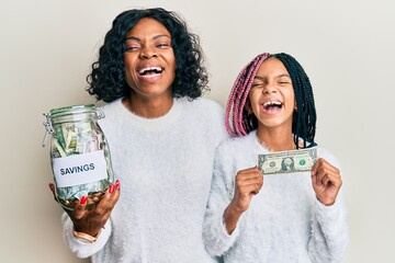 Poster - Beautiful african american mother and daughter holding jar with savings and 1 dollar banknote smiling and laughing hard out loud because funny crazy joke.