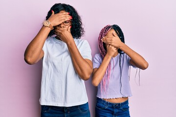 Wall Mural - Beautiful african american mother and daughter wearing casual clothes and glasses covering eyes and mouth with hands, surprised and shocked. hiding emotion