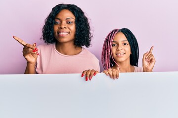 Wall Mural - Beautiful african american mother and daughter holding blank empty banner smiling happy pointing with hand and finger to the side