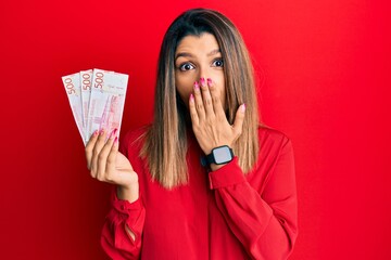 Sticker - Beautiful brunette woman holding 500 swedish krona banknotes covering mouth with hand, shocked and afraid for mistake. surprised expression