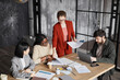 © Seventyfour - Diverse business team discussing project in black office interior focus on businesswoman wearing red jacket, copy space