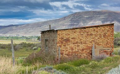 Poster - Scenic shot of a little house under construction in a green field surrounded by mountains