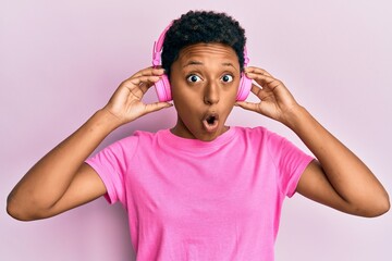 Wall Mural - Young african american girl listening to music using headphones afraid and shocked with surprise and amazed expression, fear and excited face.