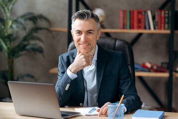 Portrait of a successful, influential, attractive caucasian gray-haired business leader, manager or lawyer, in a formal suit, sitting in the office,looking at the camera and smiling friendly