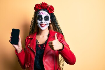 Sticker - Woman wearing day of the dead costume holding smartphone showing screen smiling happy and positive, thumb up doing excellent and approval sign