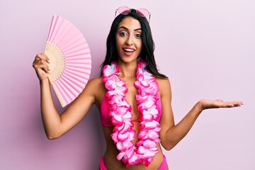 Wall Mural - Beautiful hispanic woman wearing bikini holding handfan celebrating achievement with happy smile and winner expression with raised hand