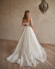 Full length portrait of young beautiful woman wearing white wedding dress. Elegant bride standing and posing against beige wall