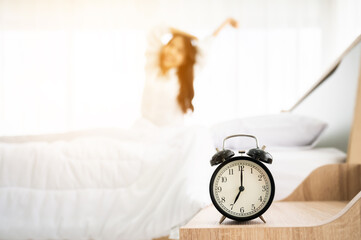 Good morning new day. Alarm clock wake up and woman sitting body stretch on bed beside window in bedroom