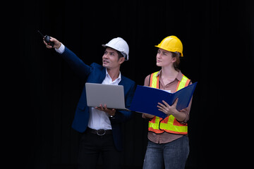 Portrait engineer and worker posing under discussion about dock container shipping , they wearing safety uniform hard hat and notebook on hand with black background.