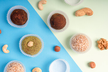 Flat lay of assortment of nut truffles or homemade organic sweet energy balls made of cashew, hazelnut, walnut and sesame ingredients laying on colorful blue and green background. Horizontal image