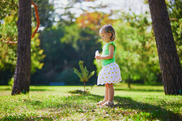 Wall Mural - Adorable toddler girl playing with bird feather and having fun in summer park. Child enjoying nature on a sunny day. Outdoor activities for kids