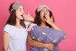 © sementsova321 - Two European women with dark hair wearing pajamas and sleeping mask, posing isolated over pink background, ladies yawning and covering mouths with palms, keeping eyes closed.
