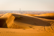 Golden Desert Dune Field Landscape With Footsteps And Transmission Towers On The Horizon, Fossil Rock, United Arab Emirates.