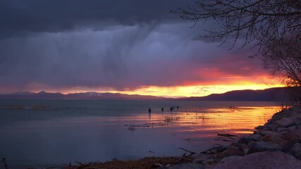 Wall Mural - Rain storm over Utah Lake as sunset fades looking towards fishermen standing in the water fishing.