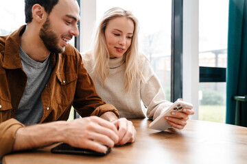 Smiling man and woman using cellphone while sitting in cafe