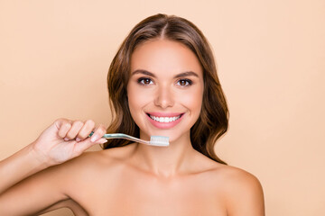 Sticker - Photo of young happy positive smiling girl with naked shoulders brushing teeth morning routine isolated on beige color background