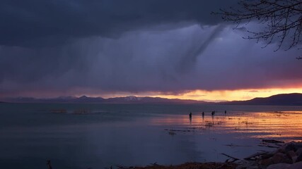 Wall Mural - Streaks of rain fall over Utah Lake at dusk past fishermen standing in the water trying to catch fish.