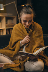 Wall Mural - woman relaxing on sofa and reading book. evening moody ambience. she is enjoying time during weekend