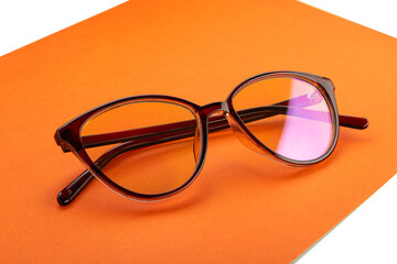 Glasses in a plastic frame with transparent lenses, on an orange sheet of paper